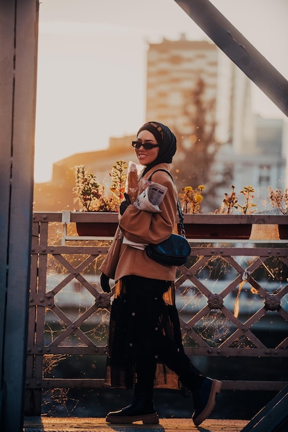 A modern Muslim woman with a hijab walks around the city while carrying a newspaper and bread in her hand.