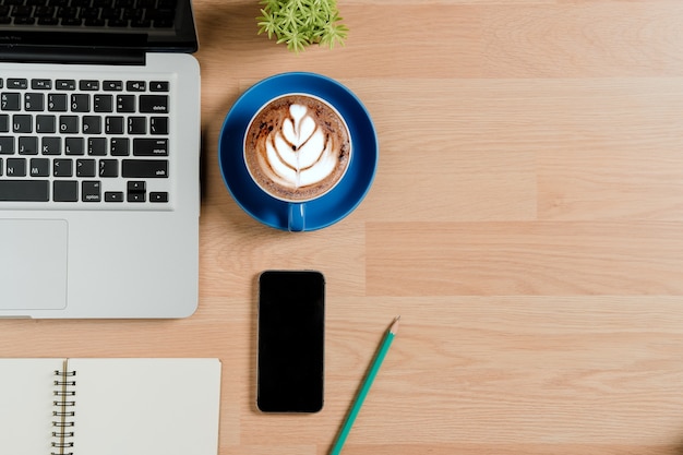 Modern office desk table with laptop computer,leather notebook,pen,smart phone and cup of 