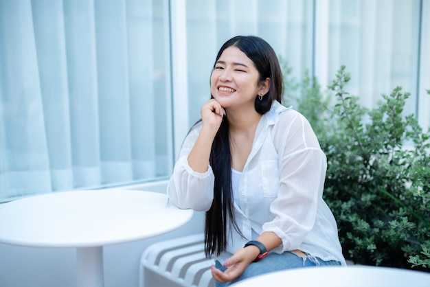 Modern portrait of beautiful happy asian woman traveler wearing smartwatch wearing beautiful white dress and wear jeans lifestyle enjoying in sitting coffee shop restaurant background