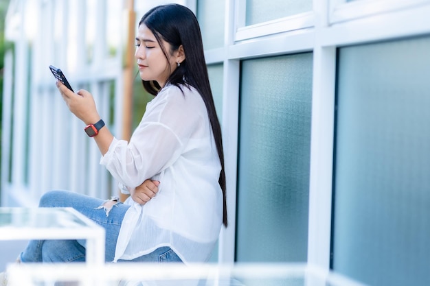 Modern portrait of happy asian woman wearing smartwatch wearing beautiful white dress and wear jeans lifestyle enjoying talking making using smartphone in sitting coffee shop restaurant background