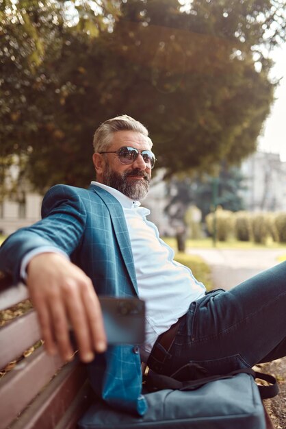 Modern senior businessman resting on a bench in the city on a break from work.