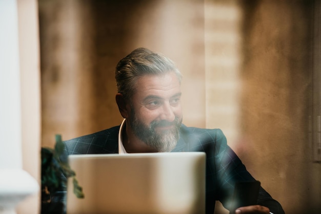 Modern senior businessman sitting in cafe and using laptop and smartphone