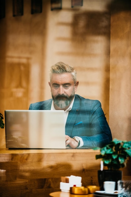 Modern senior businessman sitting in cafe and using laptop and smartphone