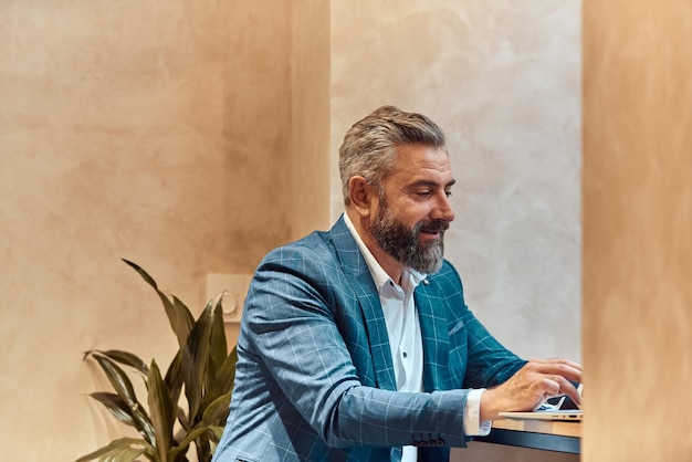 Modern senior businessman sitting in cafe and using laptop and smartphone.