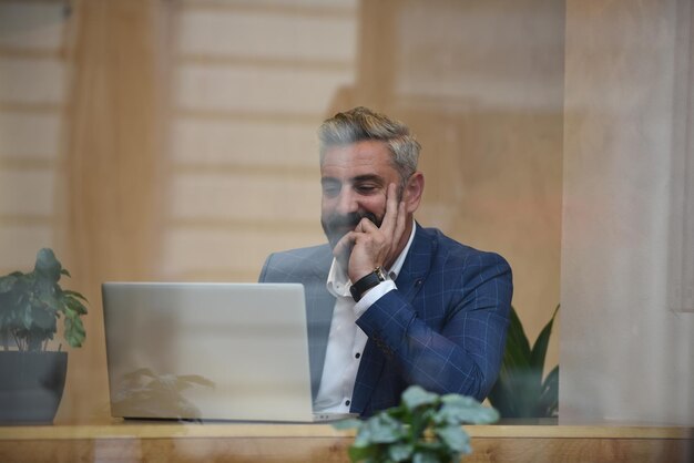 Modern senior businessman sitting in cafe and using laptop and smartphone.