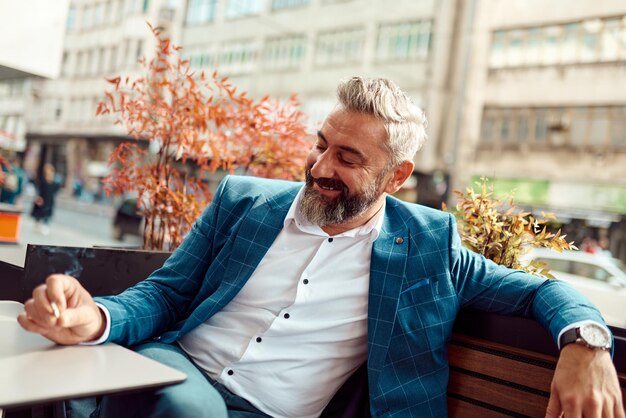 Modern senior businessman smoking a cigarette while resting in a cafe after a hard day's work.