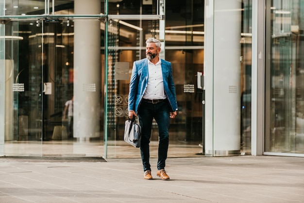 Modern senior businessman with a bag exits modern corporation