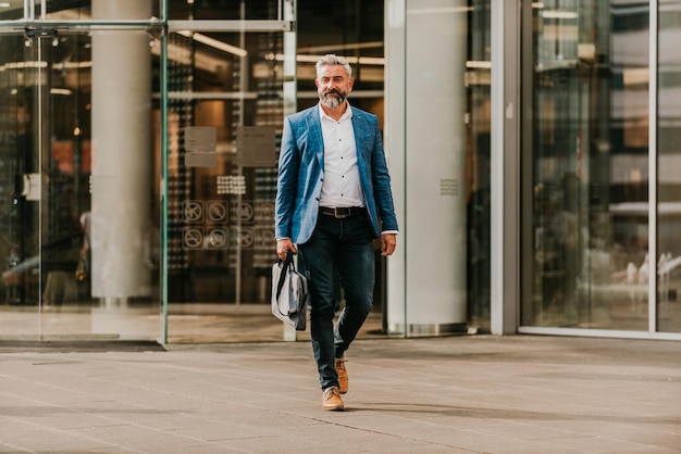 Modern senior businessman with a bag exits modern corporation