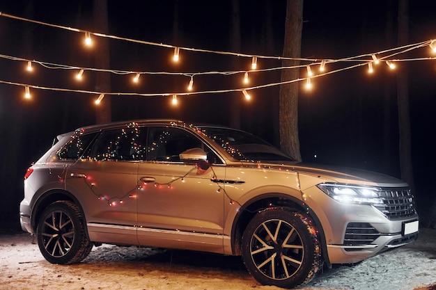 Modern silver colored automobile parked in forest with holiday decoration