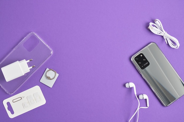 Modern smartphone and accessories on a purple background, top view, copy space, set for a smartphone, case, protective glass, headphones, charger hd camera 100x