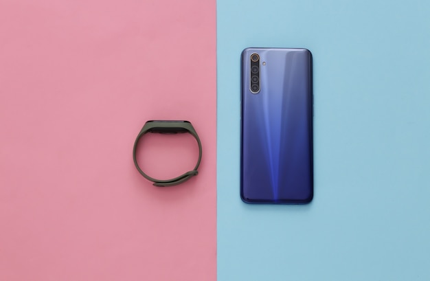 Modern smartphone and smart bracelet on a blue-pink pastel