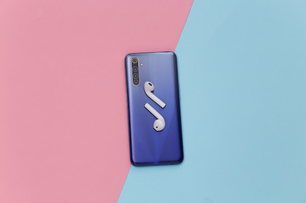 Modern smartphone with wireless earphones on blue pink pastel background.