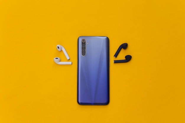 Modern smartphone with wireless earphones on yellow background.