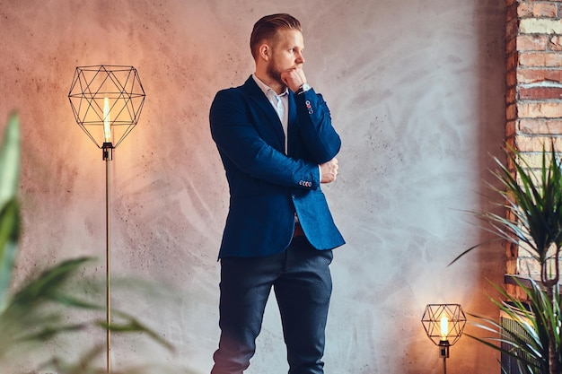 A modern, stylish male dressed in an elegant suit posing in a room with loft interior.