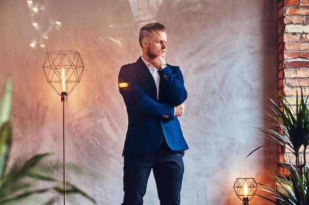 A modern, stylish male dressed in an elegant suit posing in a room with loft interior.