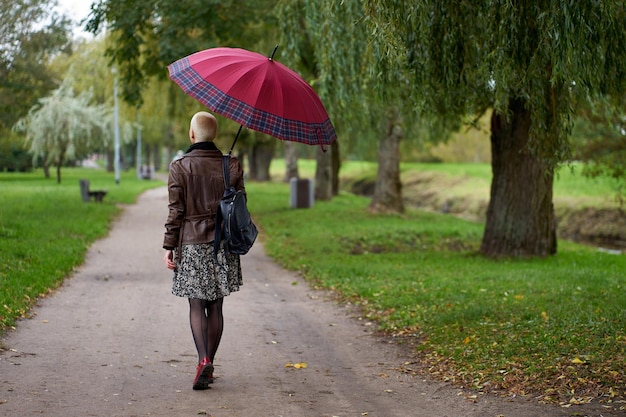 Modern stylish short haired blonde woman walks in the autumn park with red umbrella View from back