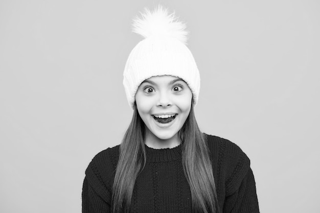 Modern teen girl wearing sweater and knitted hat on isolated yellow background