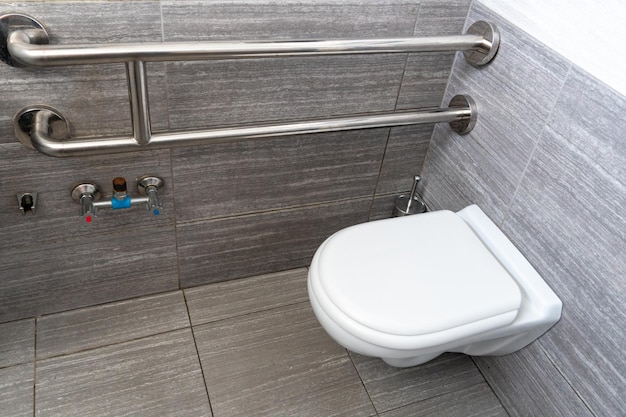 A modern toilet room with a toilet bowl and a toilet paper holder Metal vandalproof toiletries and handrails for the disabled and pensioners Interior design