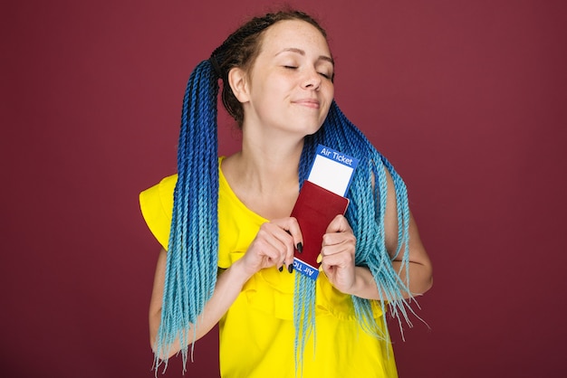 A modern trendy smiling woman in yellow dress with air tickets and a passport in her hand