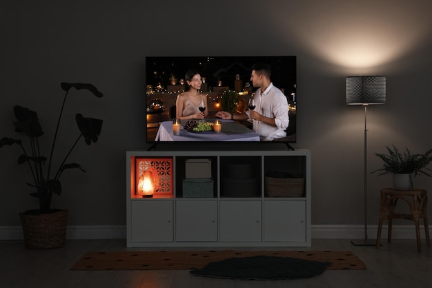 Modern TV set on wooden stand in room Scene of romantic movie on screen