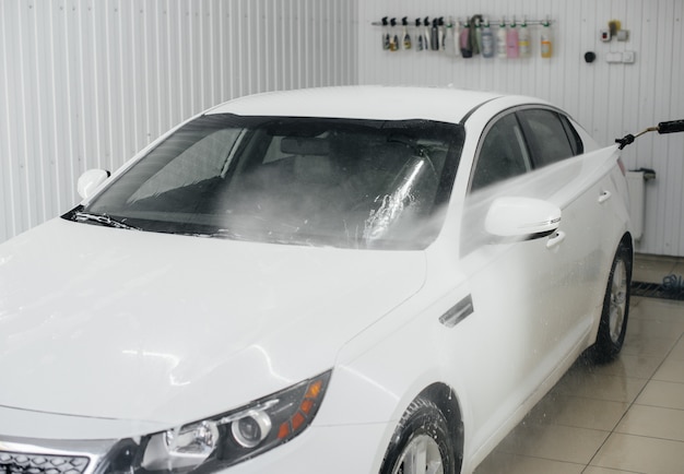 Modern washing with foam and high-pressure water of a white car. Car wash.