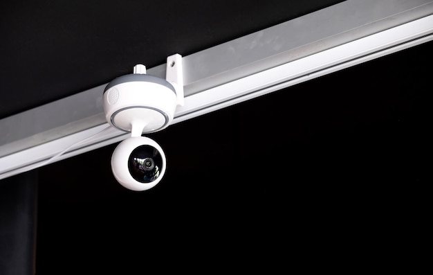 Modern white surveillance camera mounted on the ceiling in the living room to record the events that