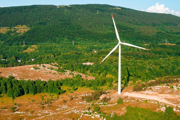 Modern wind driven generator operates producing green energy against big forestry mountain in highla...