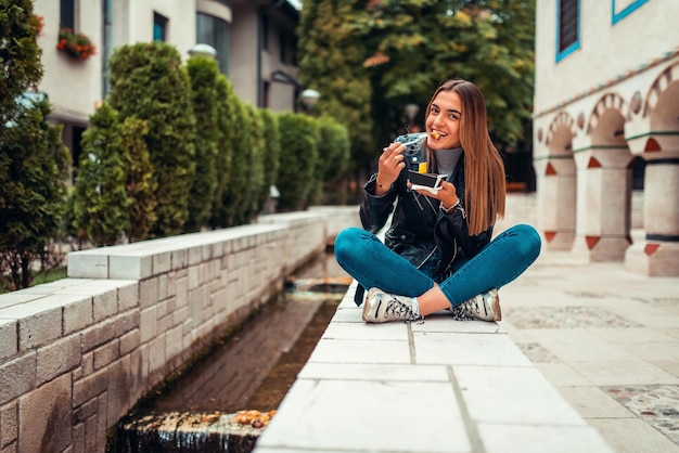 A modern woman sits in the park on a break from college and eats fresh poffertjes. Selective focus. High quality photo