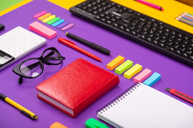 Modern working place with keyboard, diary, pencils, pens and glasses on orange-purple.