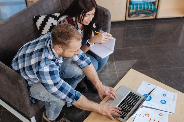 Modern workplace. Hardworking handsome young man pressing button and using a touchpad while showing something to his colleague