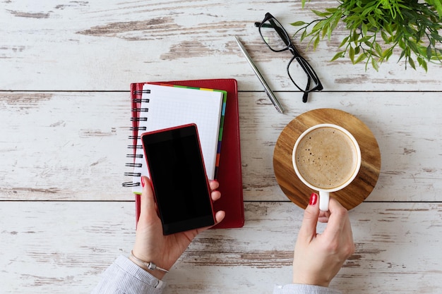 Modern workplace with woman hand using mobile phone and drinking coffee in office