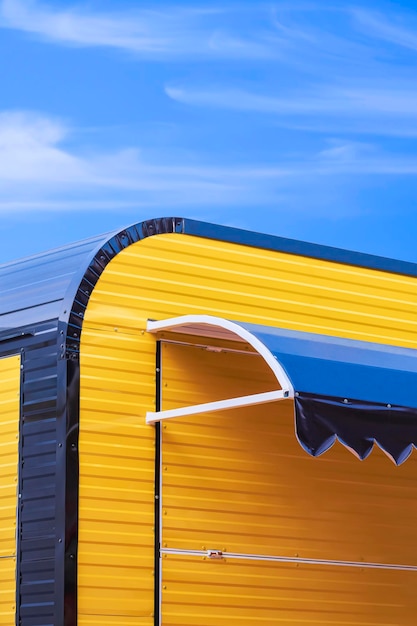 Modern yellow and black corrugated steel coffee street kiosk against blue sky background