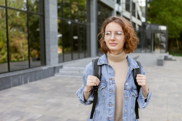 Modern young student woman in stylish denim jacket and backpack outdoors