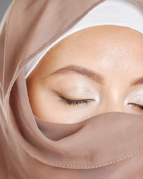 Modest arab woman wearing makeup with face covered in a brown traditional hijab Closeup of one beautiful young muslim female with radiant skin and eyes closed wearing a religious headscarf covering