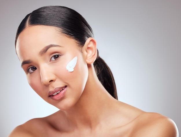 Moisturising helps your skin stay young. Studio portrait of a beautiful young woman applying moisturiser to her face against a grey background.