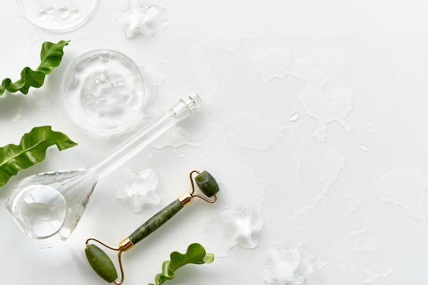 Moisturizer, green jade face roller with ice pieces. Exotic fern leaves. Minimal flat lay on off white background, copy-space . Facial massage, handmade cosmetics, top view with text place.