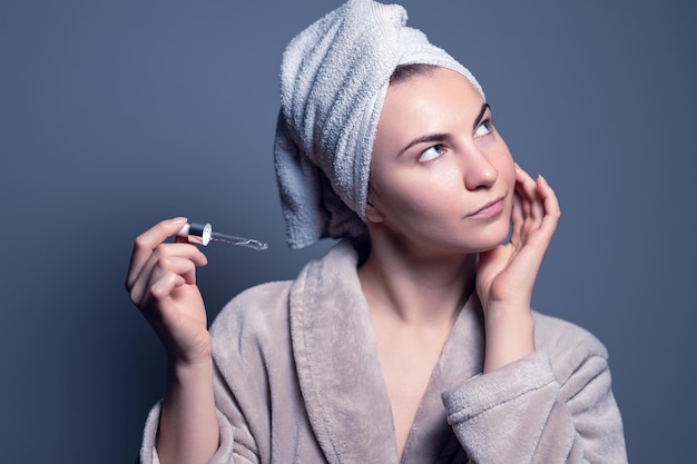 Moisturizing face serum. The girl holds a pipette near her face. Gray background. Skin care, healthy