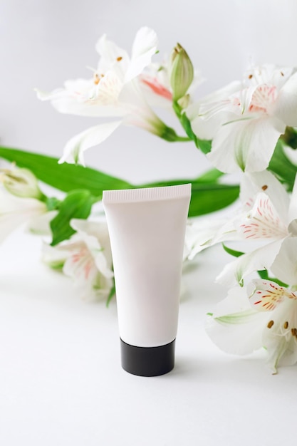 Moisturizing hand cream in a white case with a black lid on a background of alstroemeria