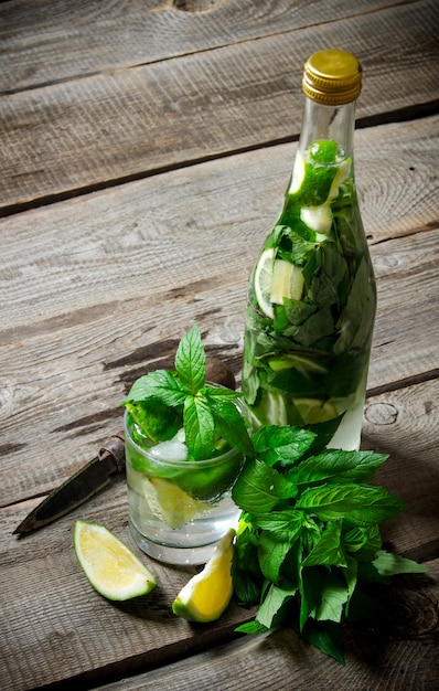 Mojito cocktail . Cocktail in glass and bottle , also mint and limes on a wooden table .