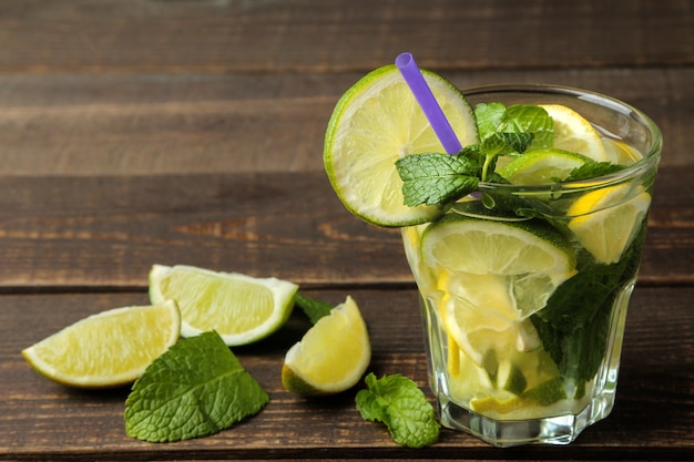 Mojito cocktail in a glass with lime, mint and lemon on a wooden brown table