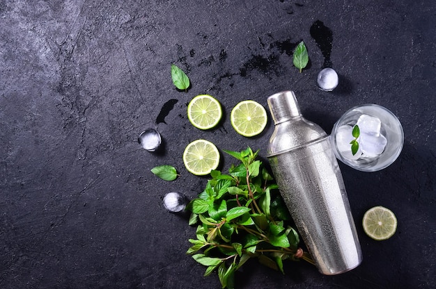 Mojito Cocktail Making Mint Lime Ice Glass and Bar Shaker on Dark Stone Table Copy Space For Your Text