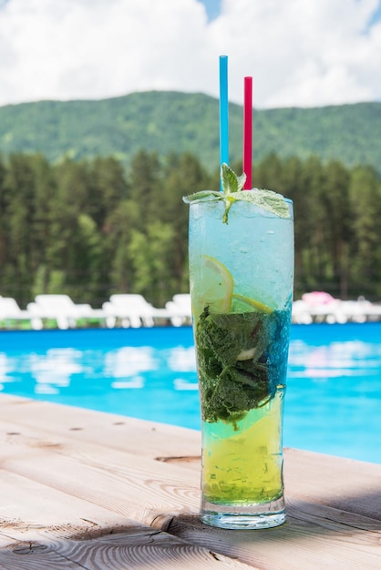 Mojito cocktail with lime and mint in highball glass at the swiming pool on summer mountain backgrou