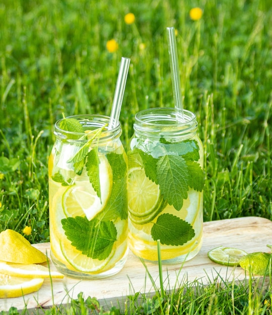 Mojito in glass jars with lemon lime and mint stands on a wooden stand on the lawn