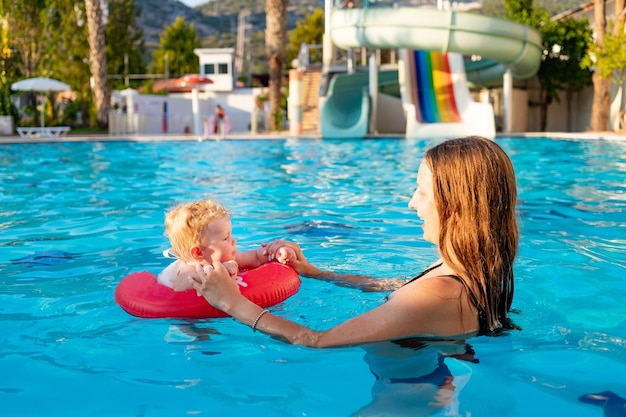 Mom and baby in an inflatable circle in the pool with water slides in the summer have fun swimming, relaxing and spending time, mom teaches the child to swim