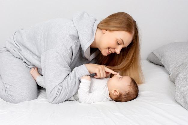 Mom and baby play on the bed Mother and son happy family beautiful blonde girl and cute baby at home