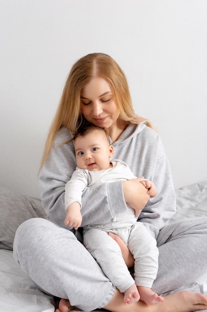 Mom and baby play on the bed Mother and son happy family beautiful blonde girl and cute baby at home