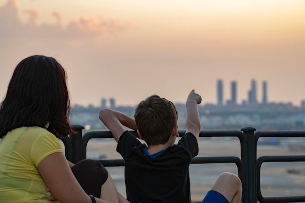 Mom and child looking at Madrid city skyline view on sunset.Kid pointing out the 4 towers silhouette