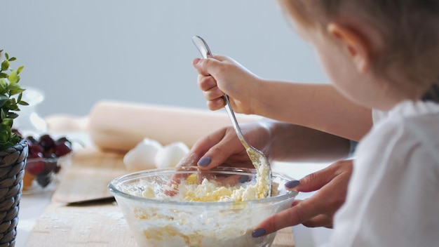 Mom and child puts the sugar and mixing the dough for pancakes