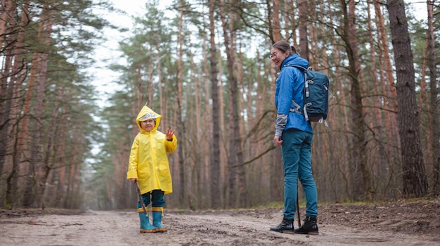 Mom and child walk in the forest road after rain in raincoats together