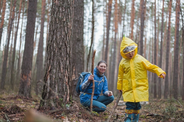 Mom and child walking in the forest after rain in raincoats together